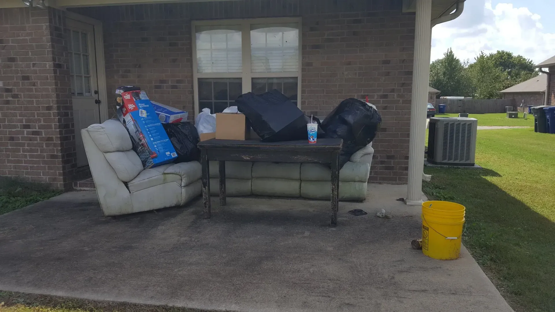 A couch , chair , table , and trash bags are outside of a brick house.