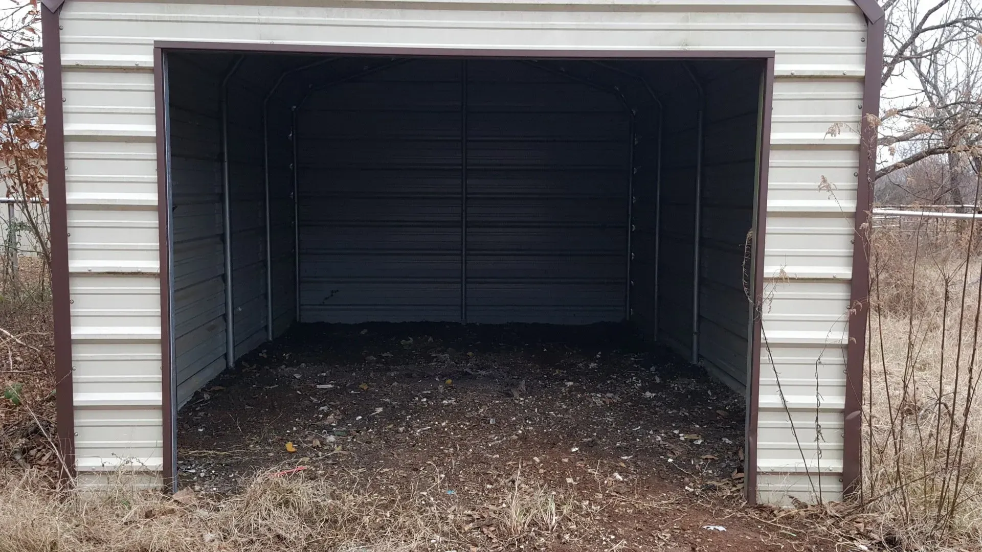 An empty garage with a door open in a field.