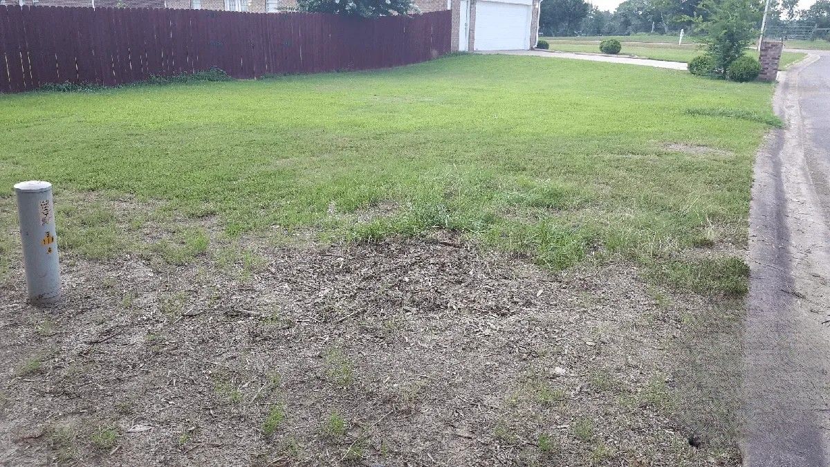 A lawn with a red fence and a drain pipe in the middle of it.