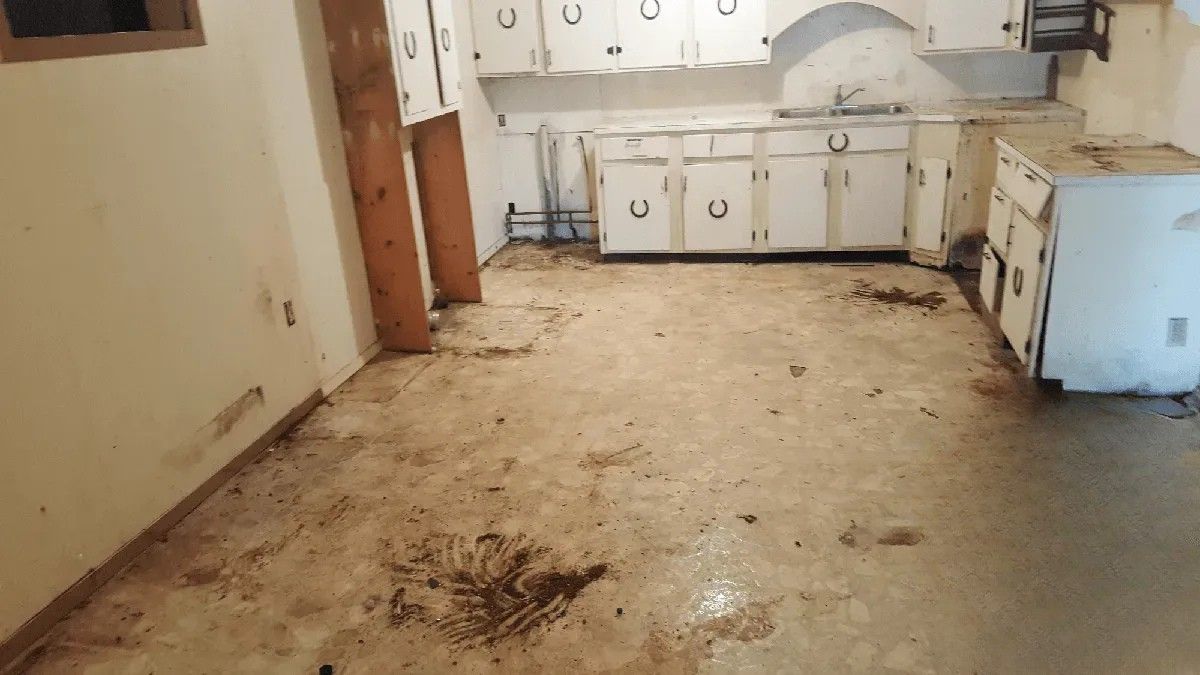 A dirty kitchen with white cabinets and a dirty floor.