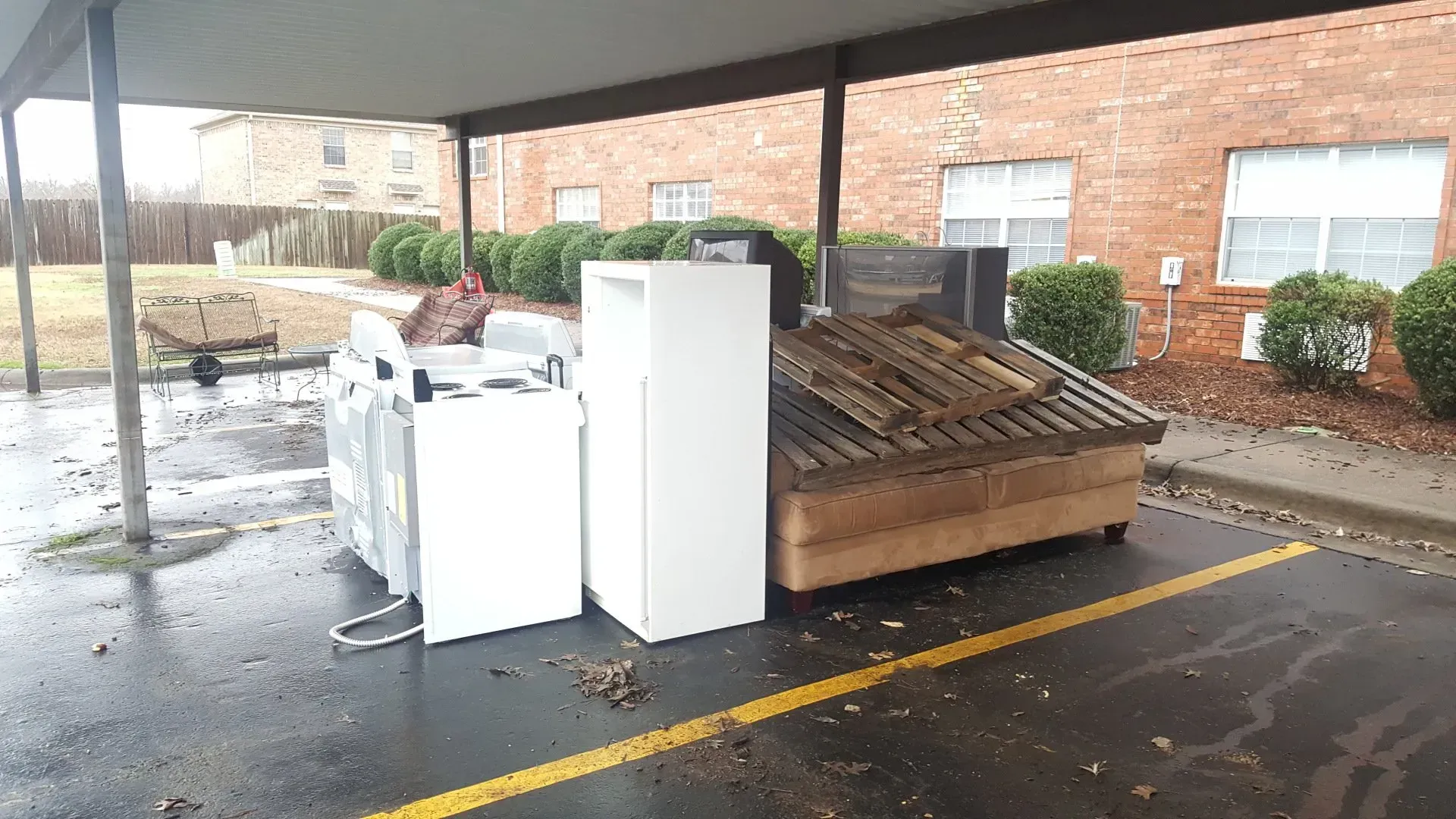 A bunch of appliances are in a parking lot under a canopy