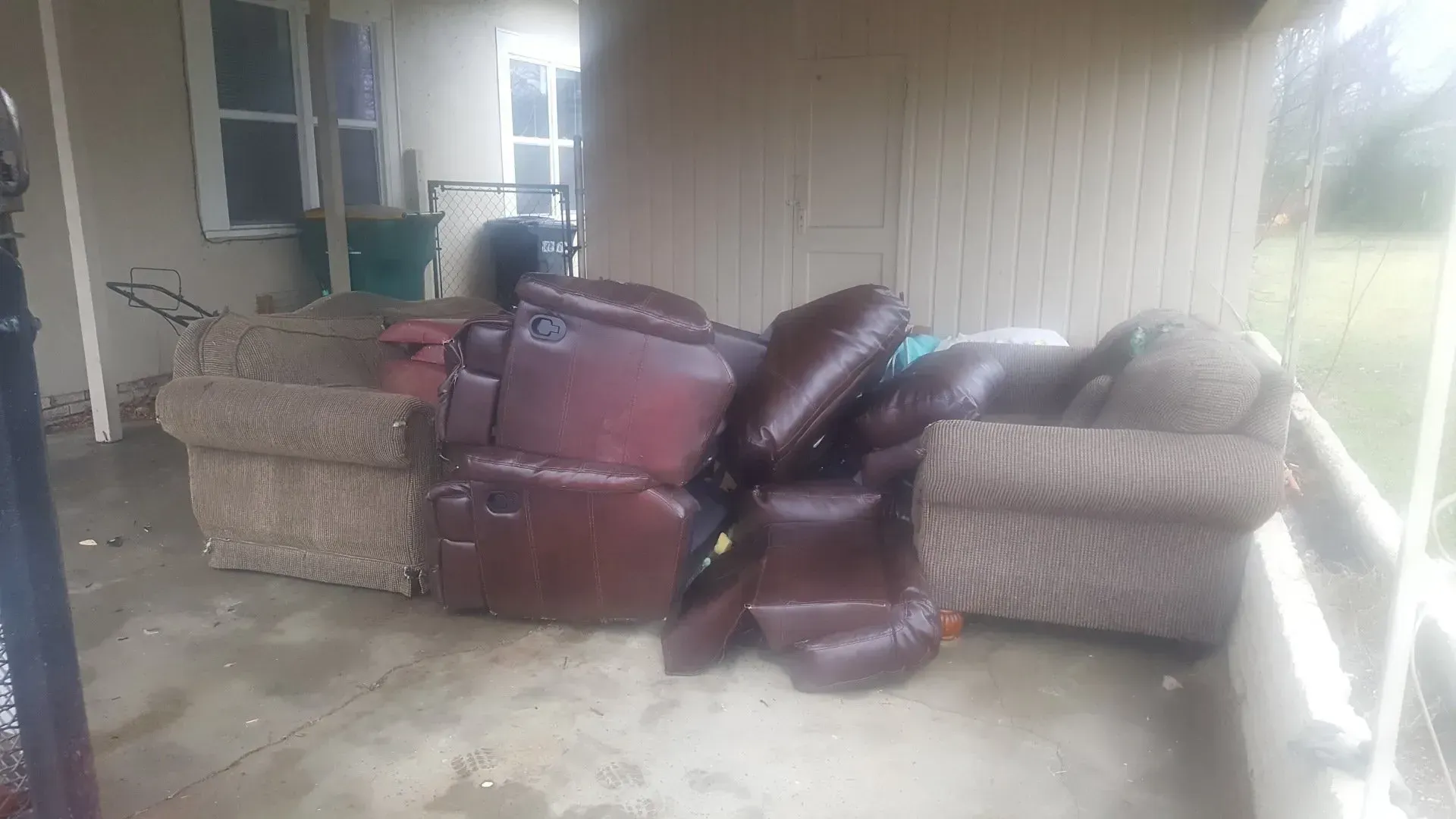 A pile of furniture is sitting on the ground outside of a house.