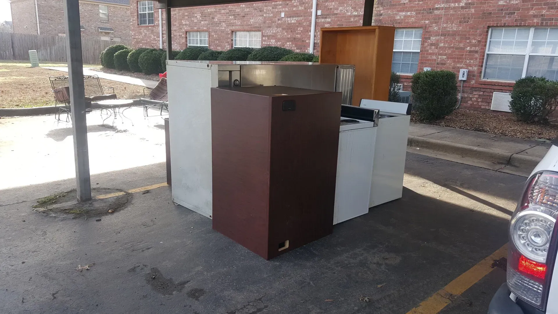 A bunch of appliances are sitting in a parking lot in front of a brick building