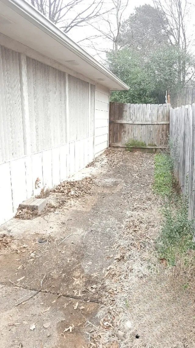 A dirt path leading to a house with a wooden fence.