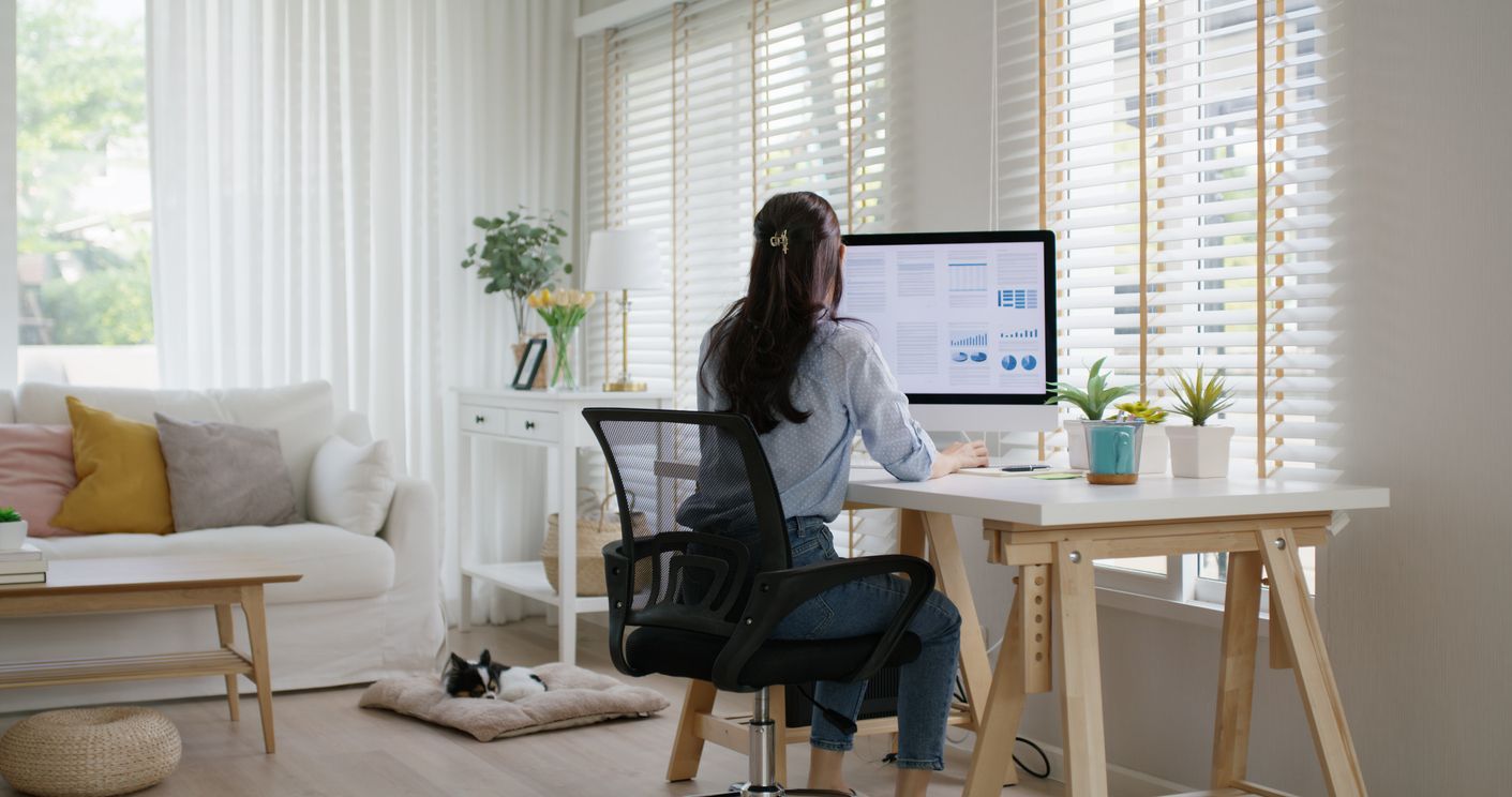 A woman is sitting at a desk in front of a computer in a living room.