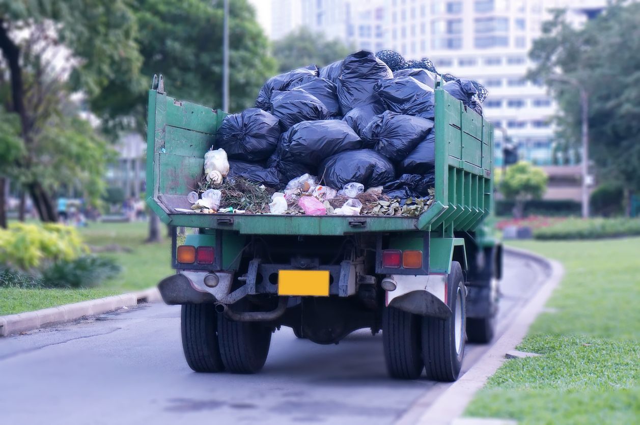 A dump truck is driving down a street filled with garbage bags.