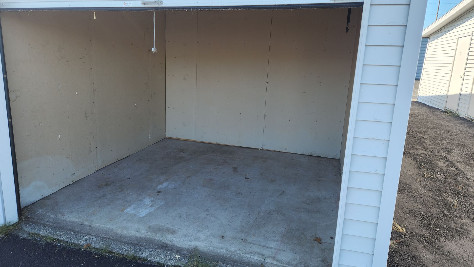 Empty storage unit with an open doorway. The interior has tan walls and a concrete floor.