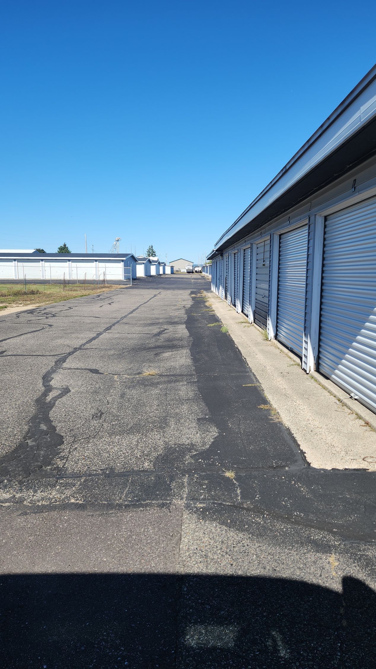 Storage units along a cracked asphalt path under a clear blue sky. Storage units along a cracked asphalt path under a clear blue sky.