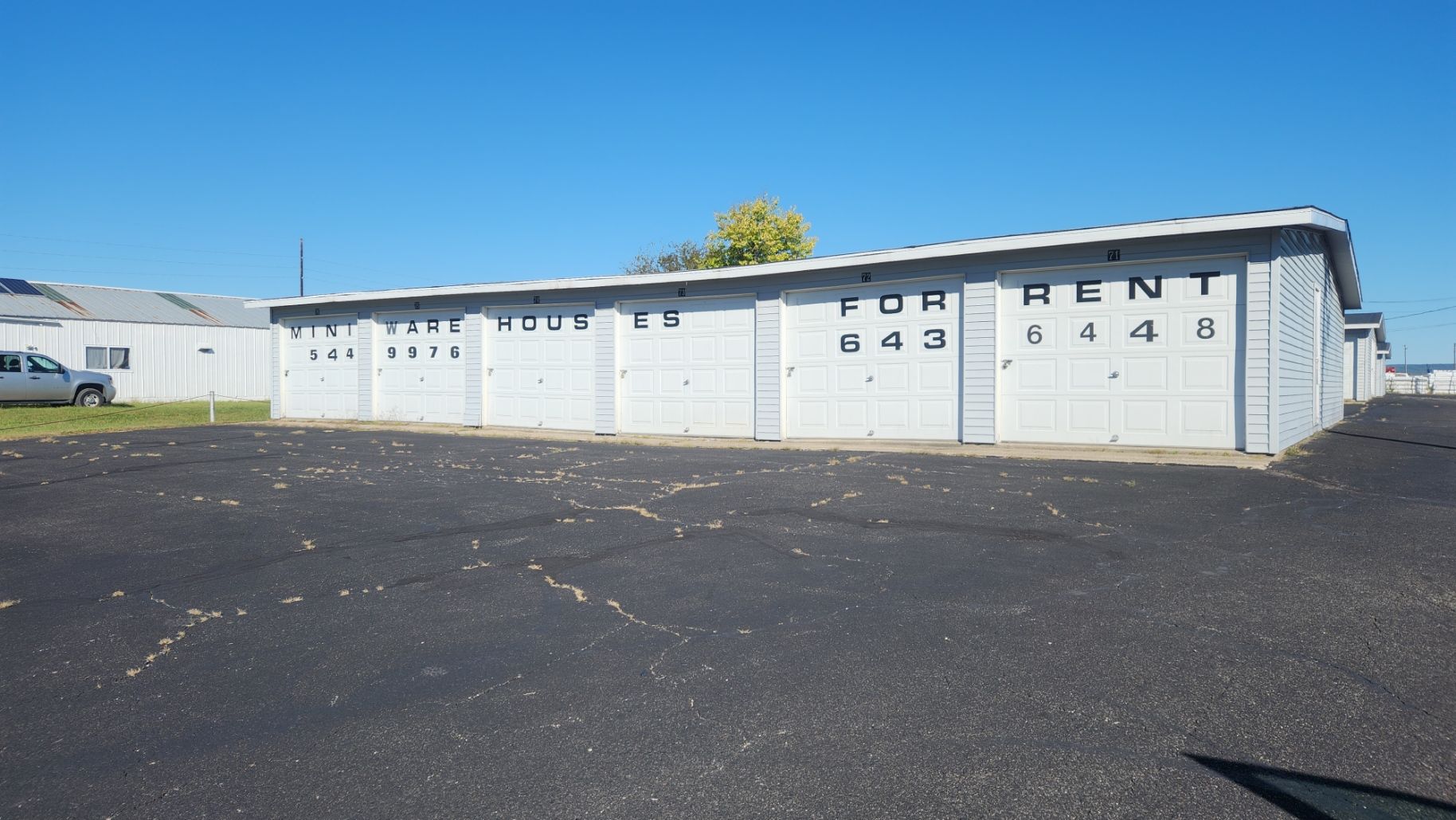 Storage units for rent on a sunny day. Gray concrete buildings with black asphalt parking lot.