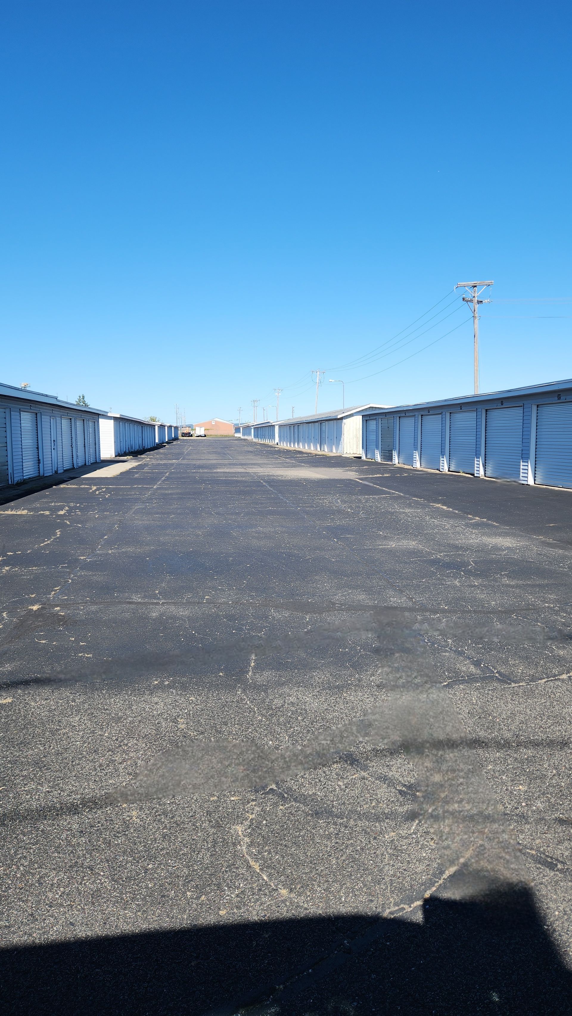 Rows of storage units with dark asphalt path, bright blue sky.