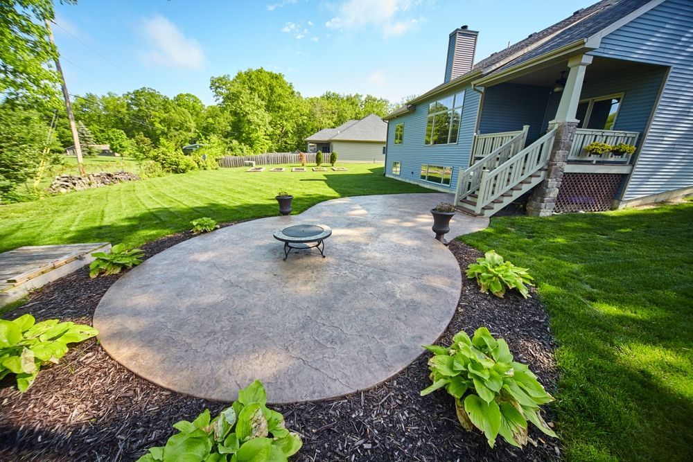 A circular patio with a fire pit in the middle of it in front of a house.