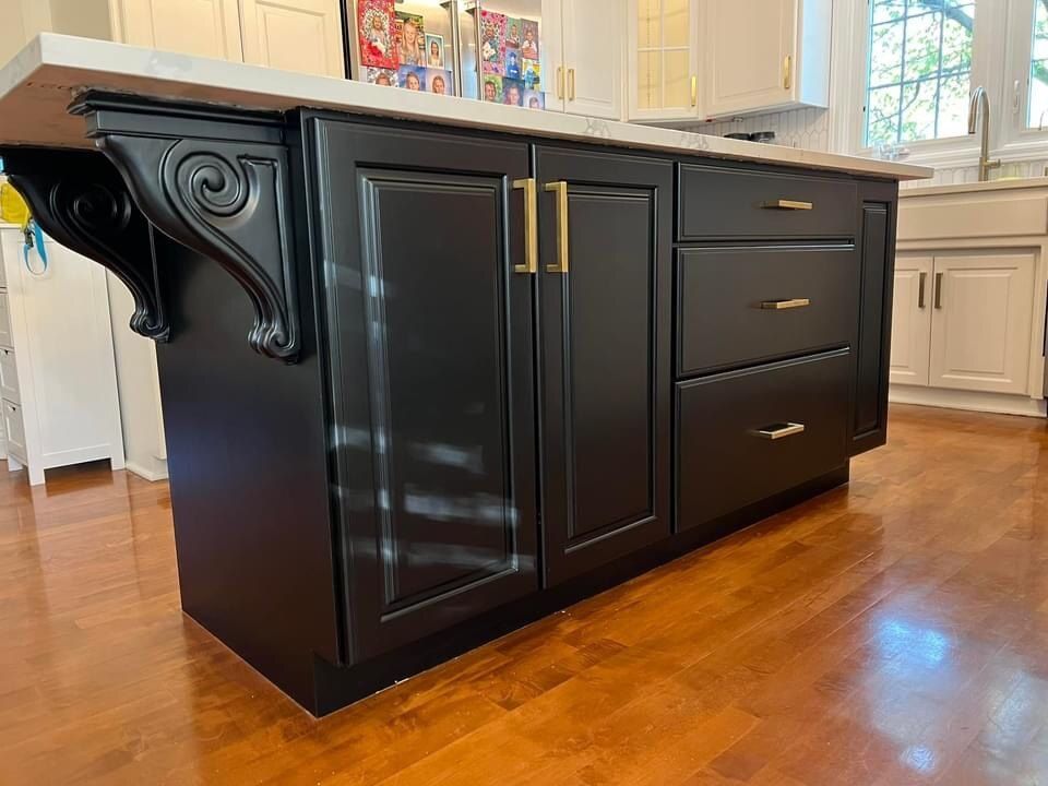 Black kitchen island with gold hardware and a white countertop, on hardwood floors.