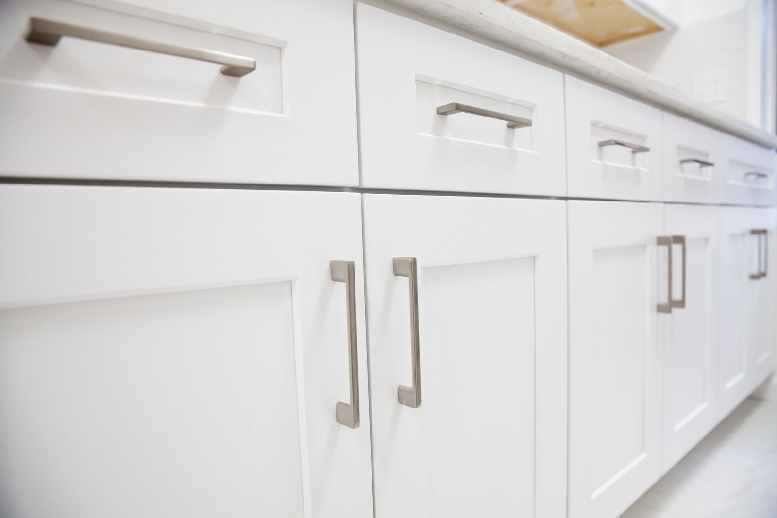 A kitchen with white cabinets and drawers with stainless steel handles.