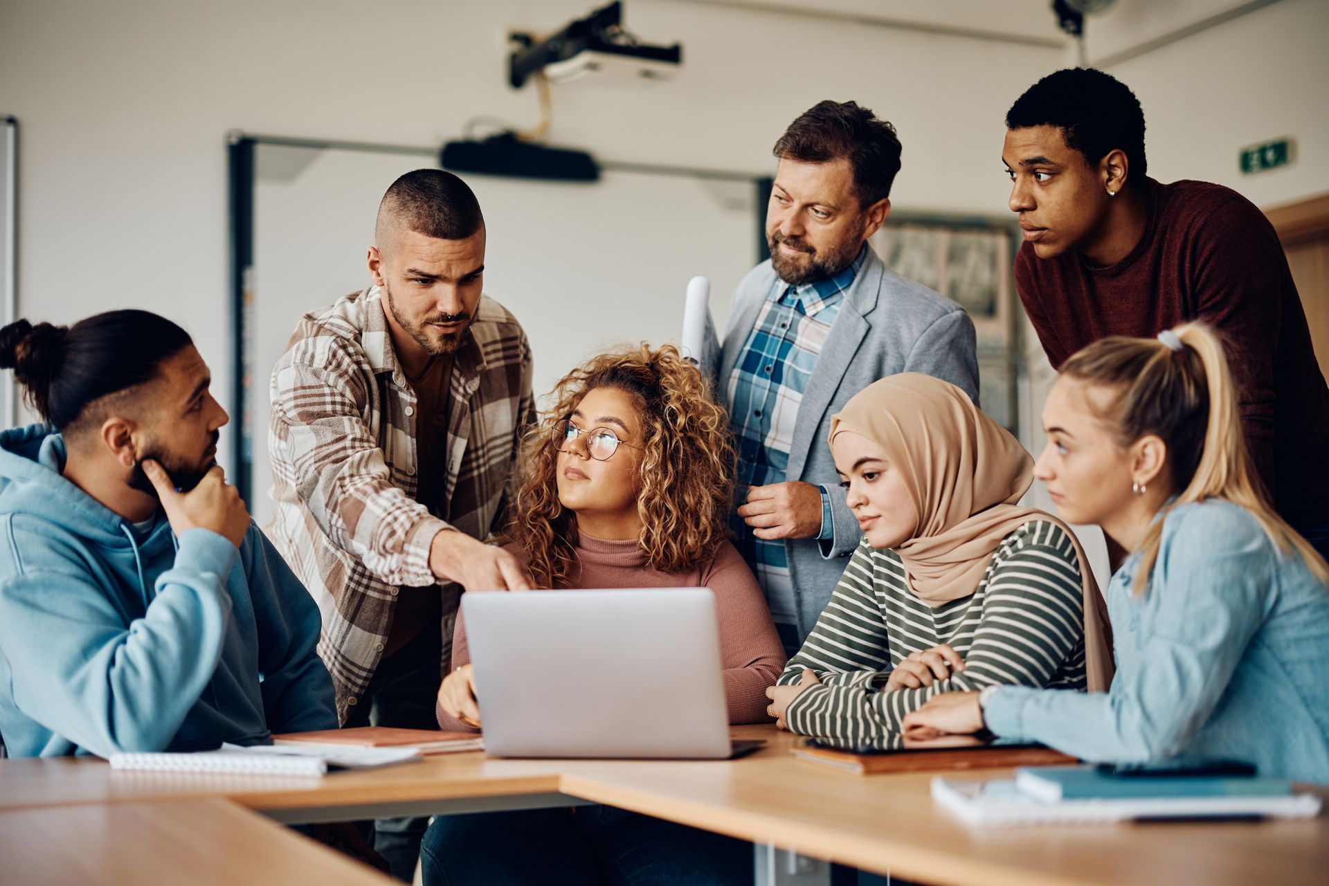 Group of coworkers gathered around a laptop in a meeting room, discussing a project together.