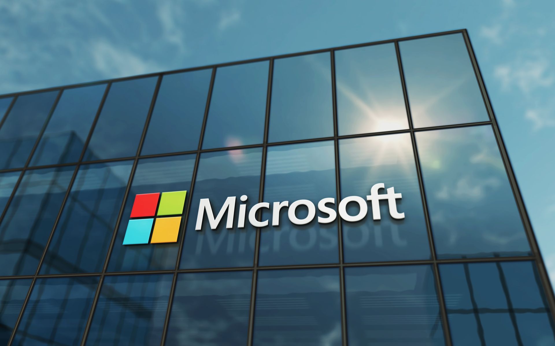 Microsoft logo on a glass office building facade under a blue sky
