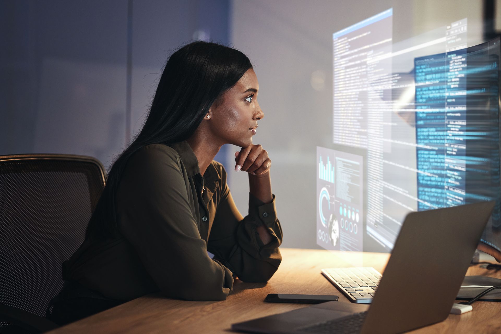 Person at a desk studying code on multiple glowing monitors in a dim office