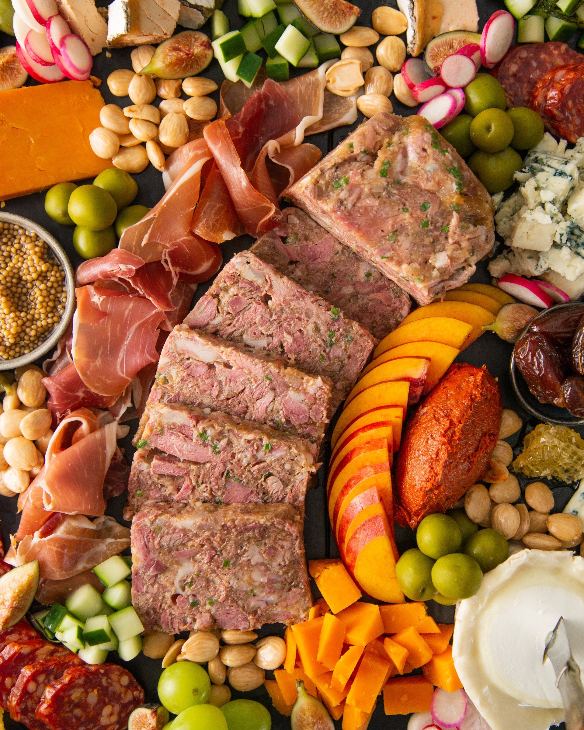overhead image of charcuterie board with head cheese, chopped, vegetables, olives and cheese