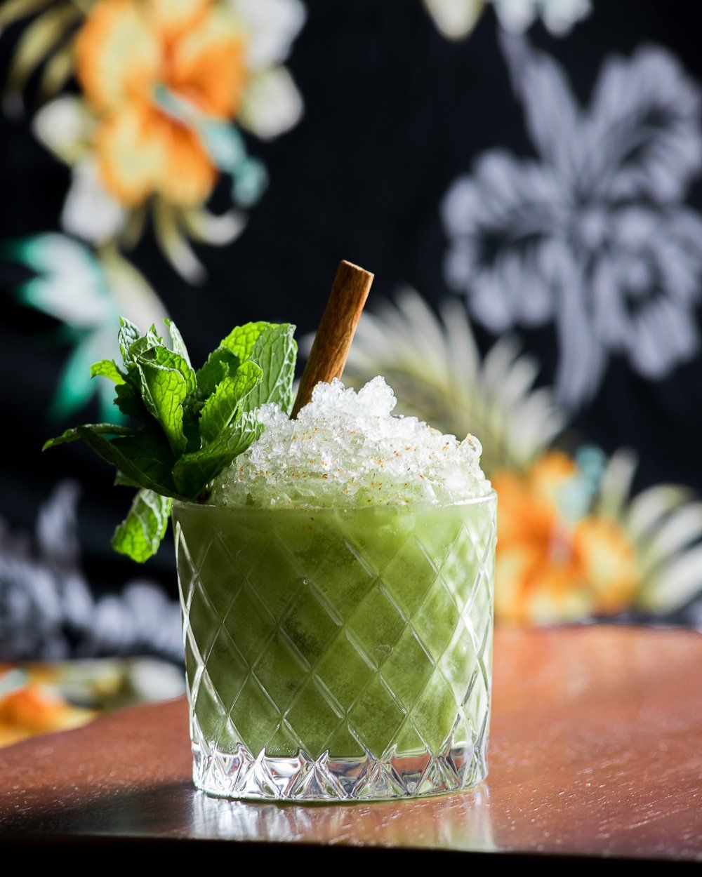 highball glass filled with crushed ice and green liquid, topped with mint and a cinnamon stick