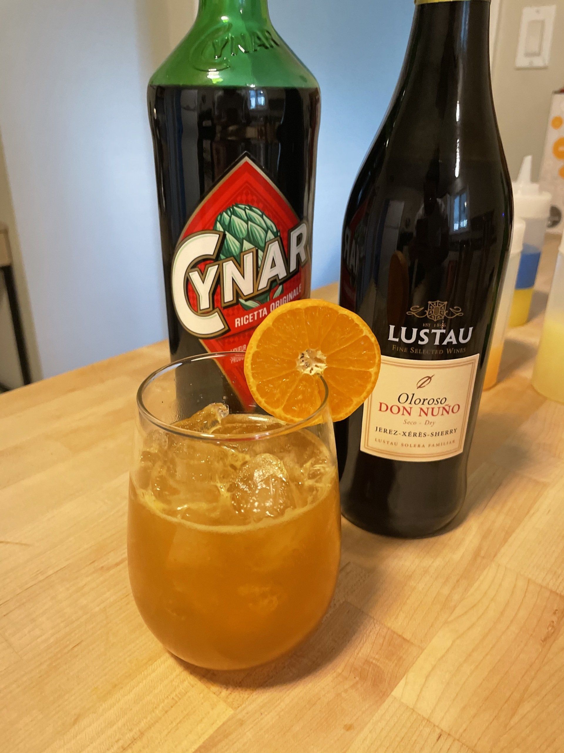 orange cocktail with bottles of sherry and cynar in the background