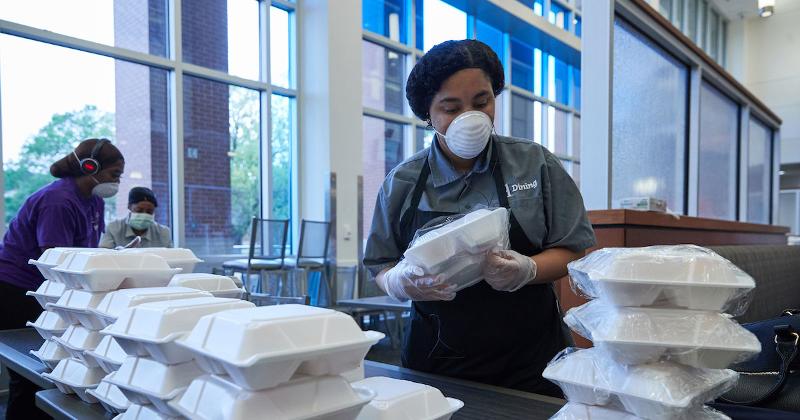 foodservice worker in a mask with takeout containers stacked in front