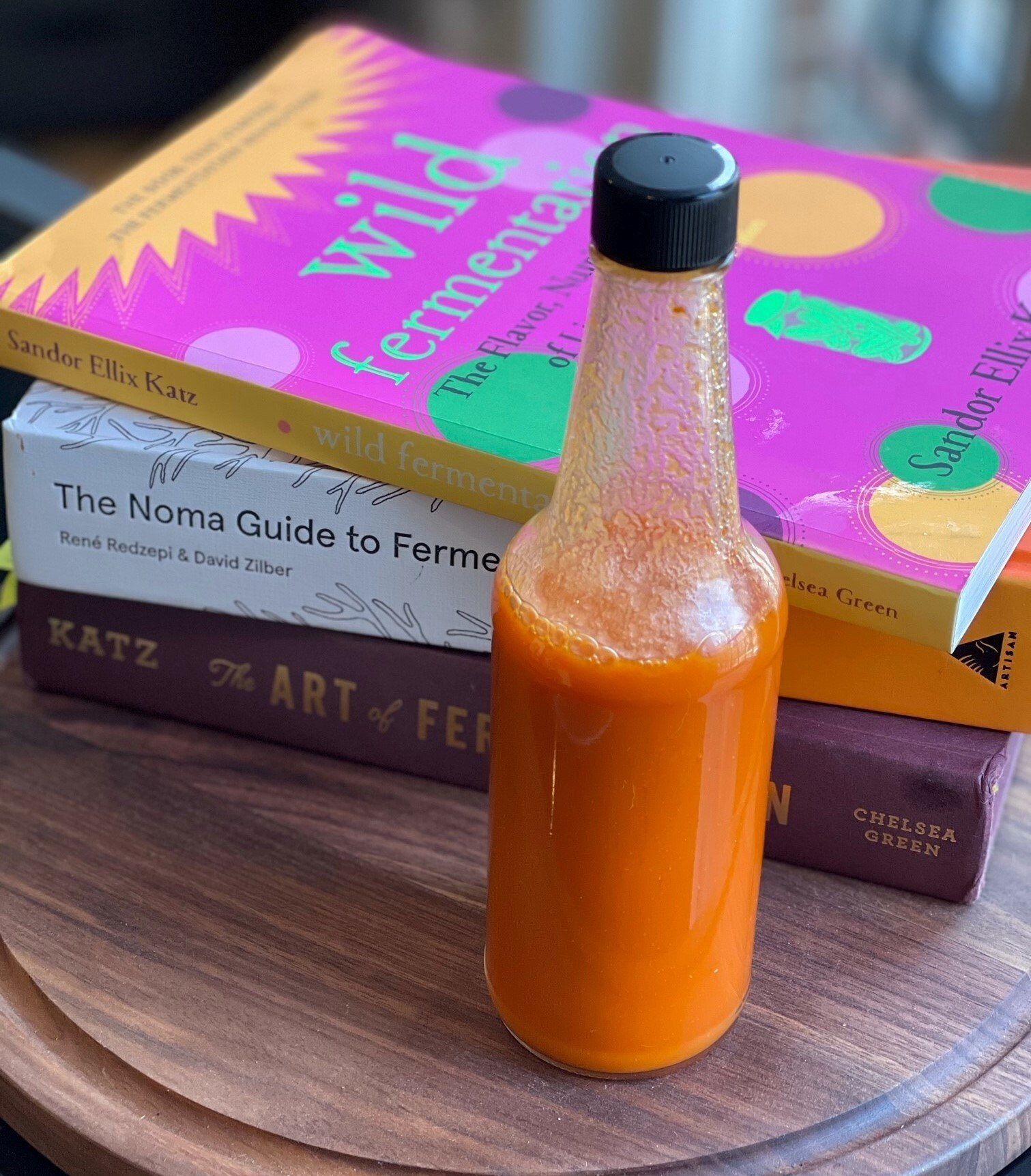 bottle of orange-colored hot sauce with books in the background