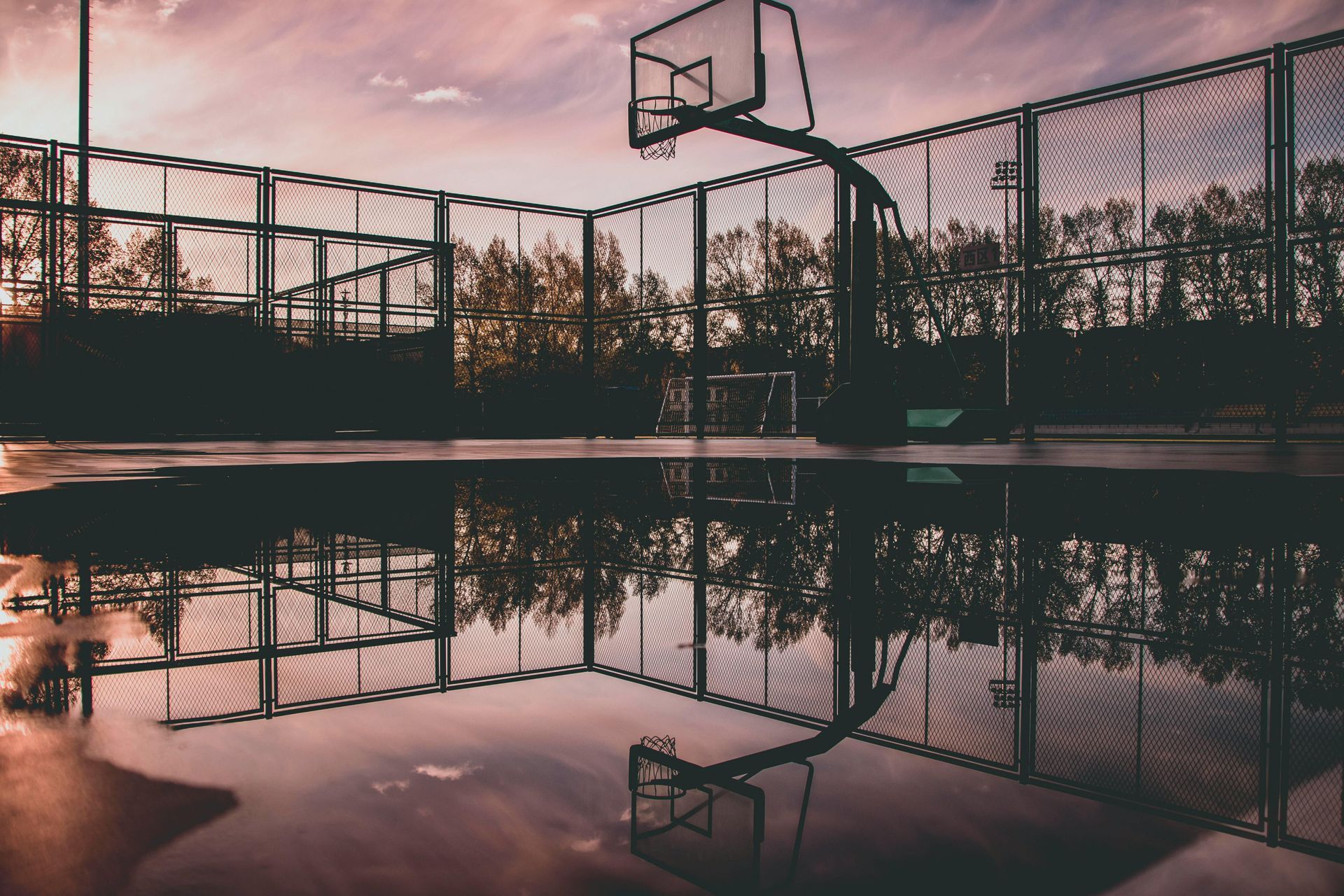A basketball hoop is reflected in a puddle of water.