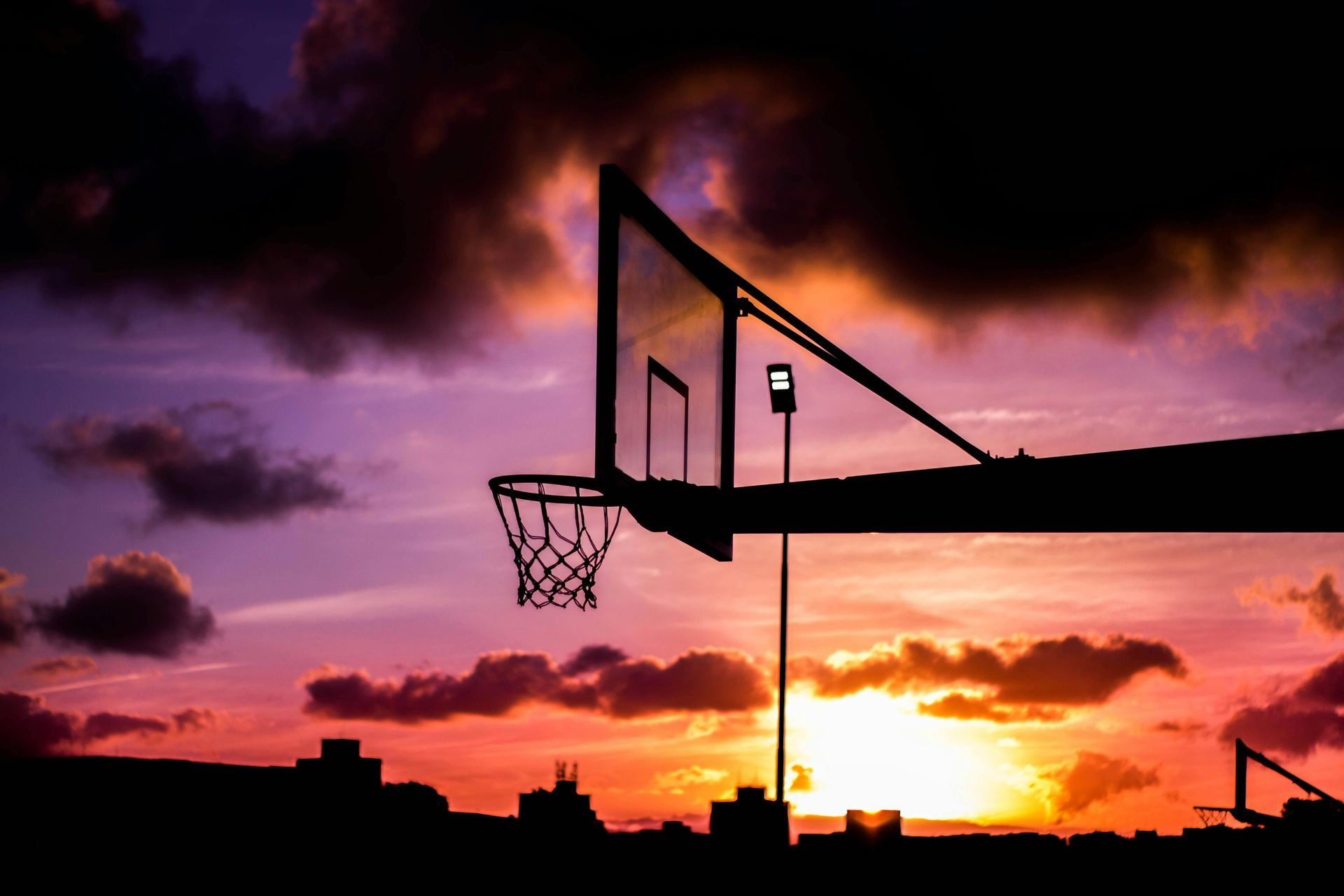 A basketball hoop is silhouetted against a sunset sky