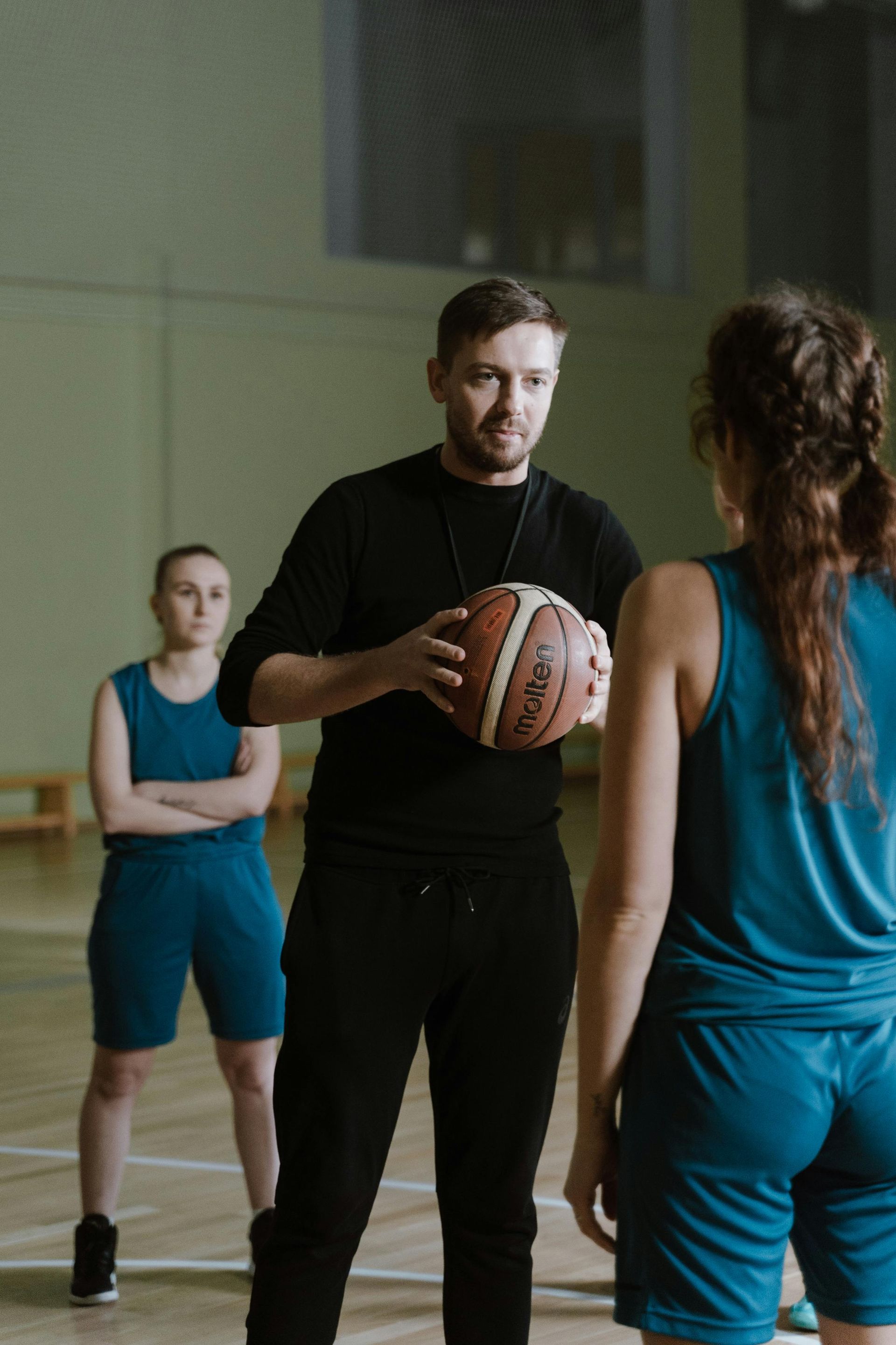 A man is holding a basketball and talking to a group of female basketball players.