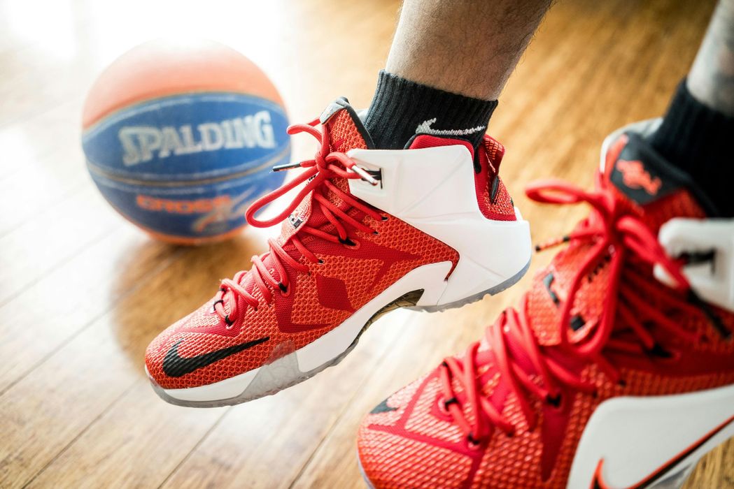 Picture of a basketball players feet wearing white and orange sneakers while jumping in the air. 