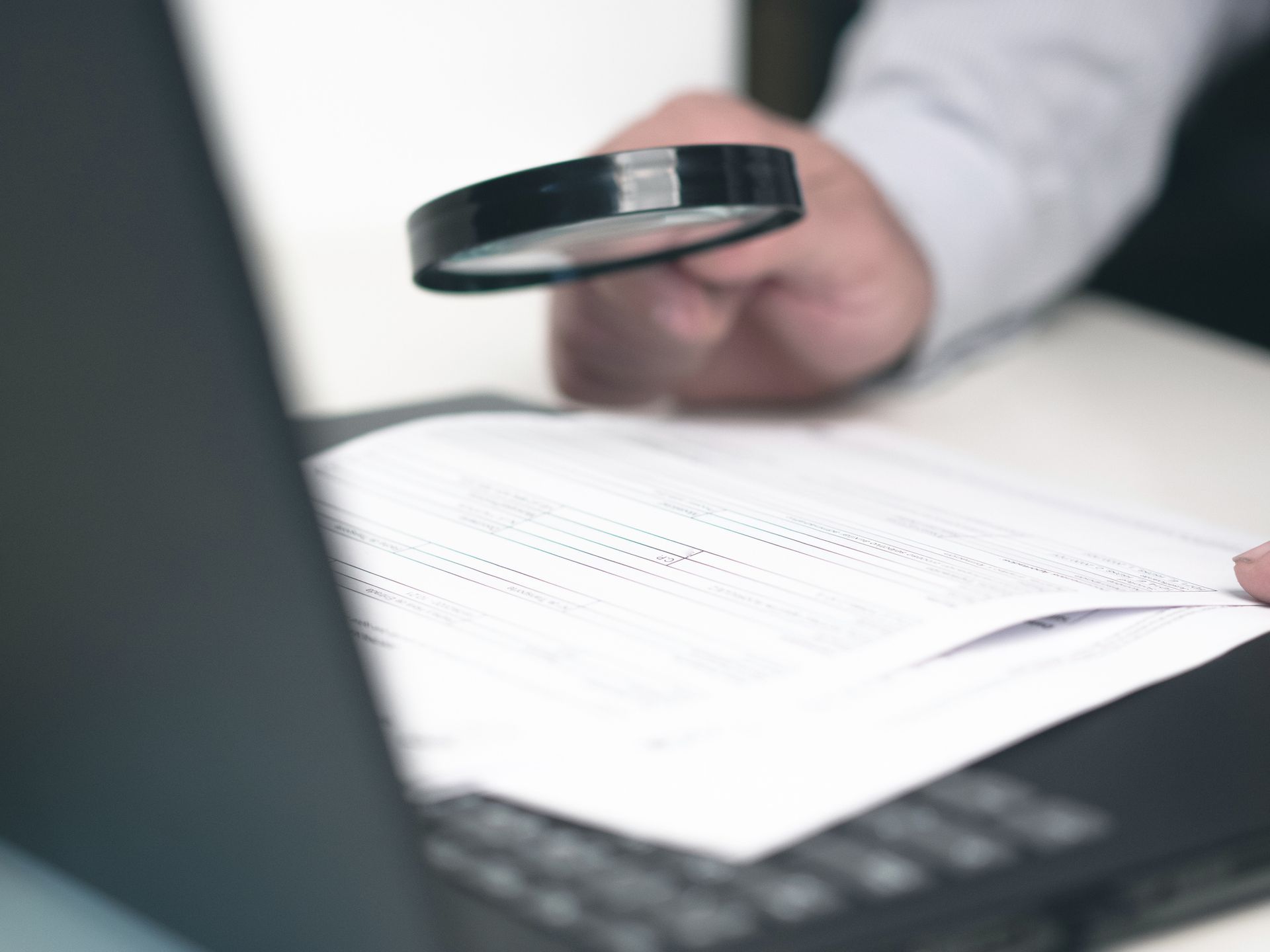 Close-up of a magnifying glass being held by a hand while poring over a document. Close-up of a magnifying glass being held by a hand while poring over a document.