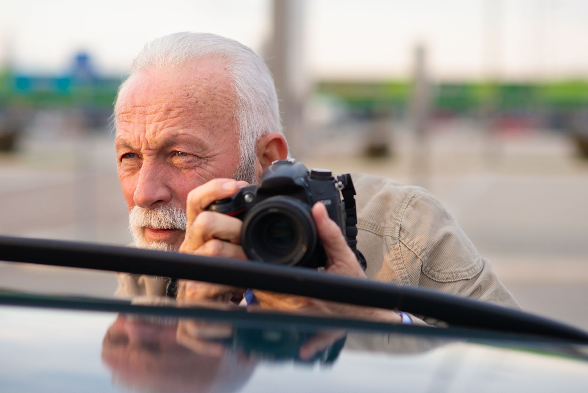 A senior white man photographing someone while hiding behind his car A senior white man photographing someone while hiding behind his car