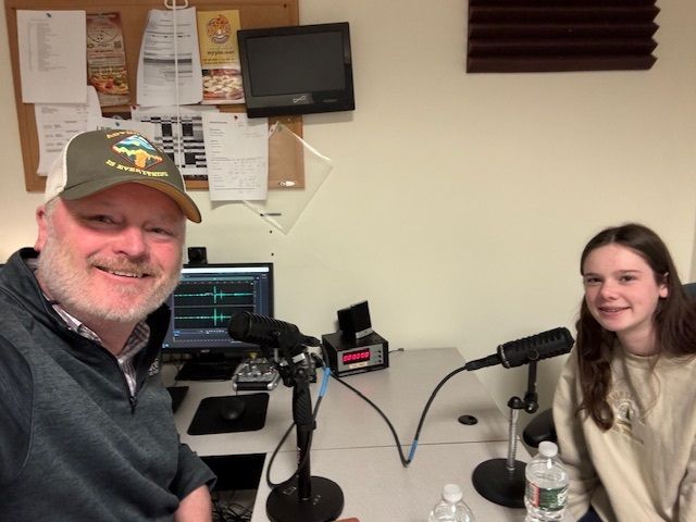 Man and young woman in a recording studio, smiling at the camera, ready to record a podcast.