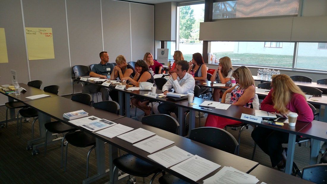 A group of people are sitting at long tables in a classroom.