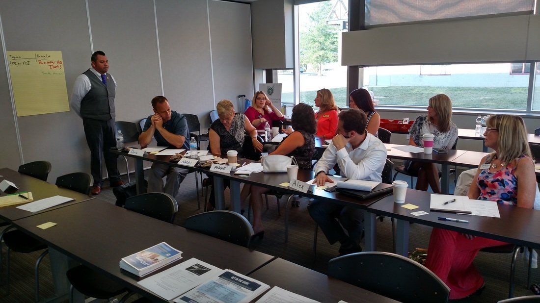 A group of people are sitting at tables in a classroom.