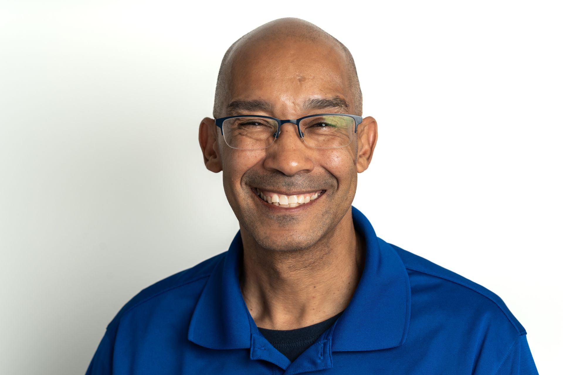 A bald man wearing glasses and a blue shirt is smiling for the camera.