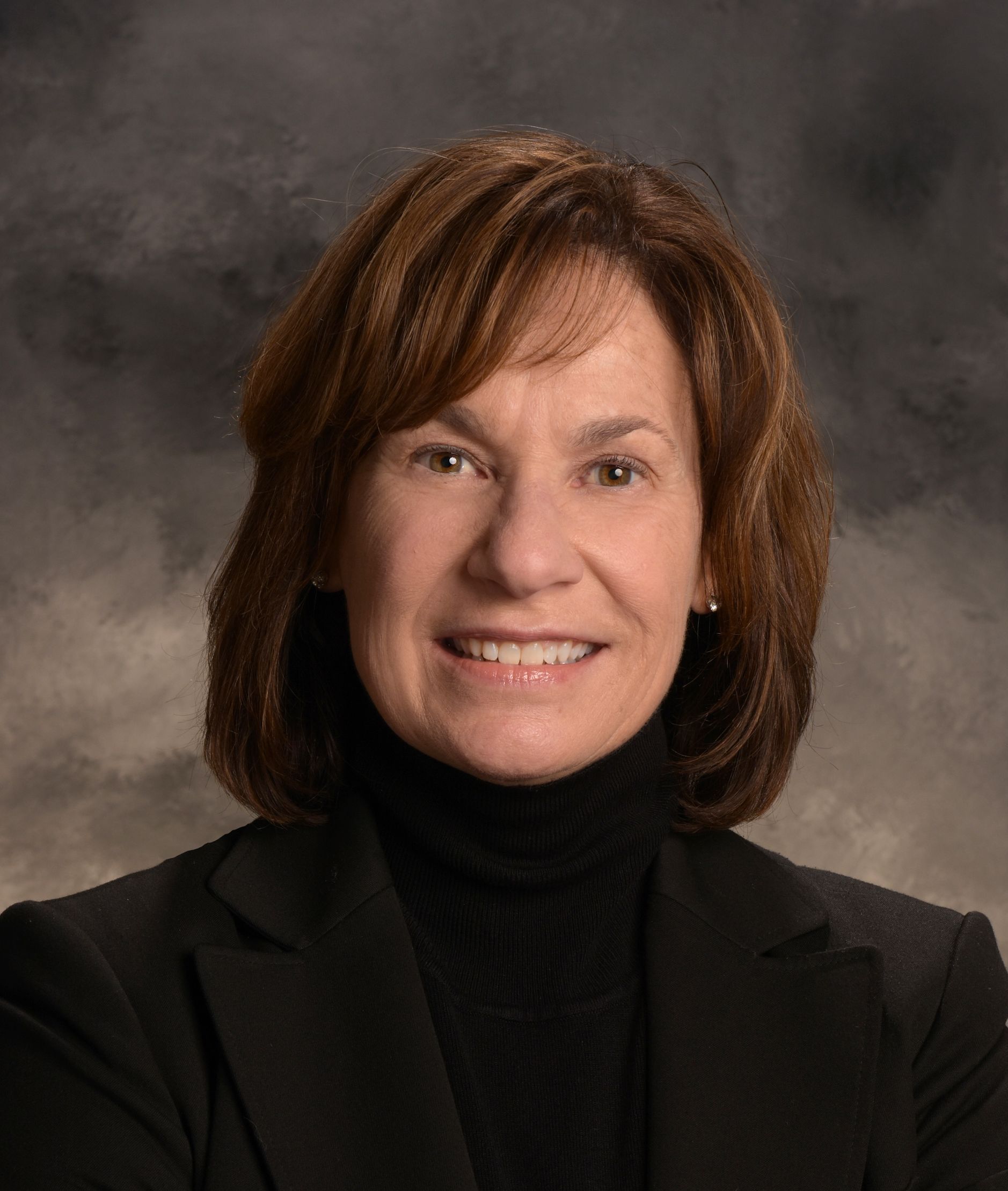 A woman wearing a black jacket and turtleneck smiles for the camera.