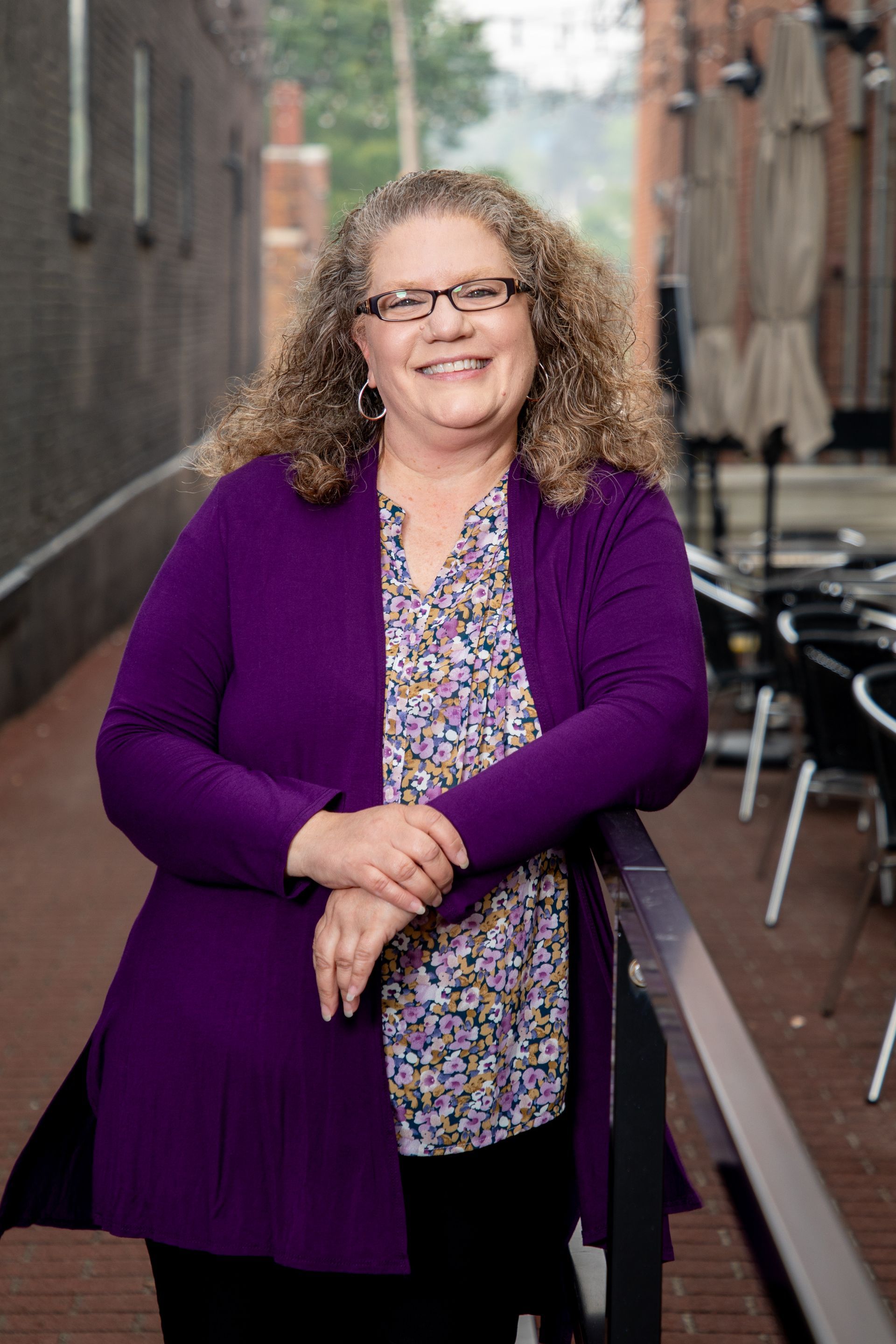 A woman in a purple sweater and glasses is standing next to a railing.