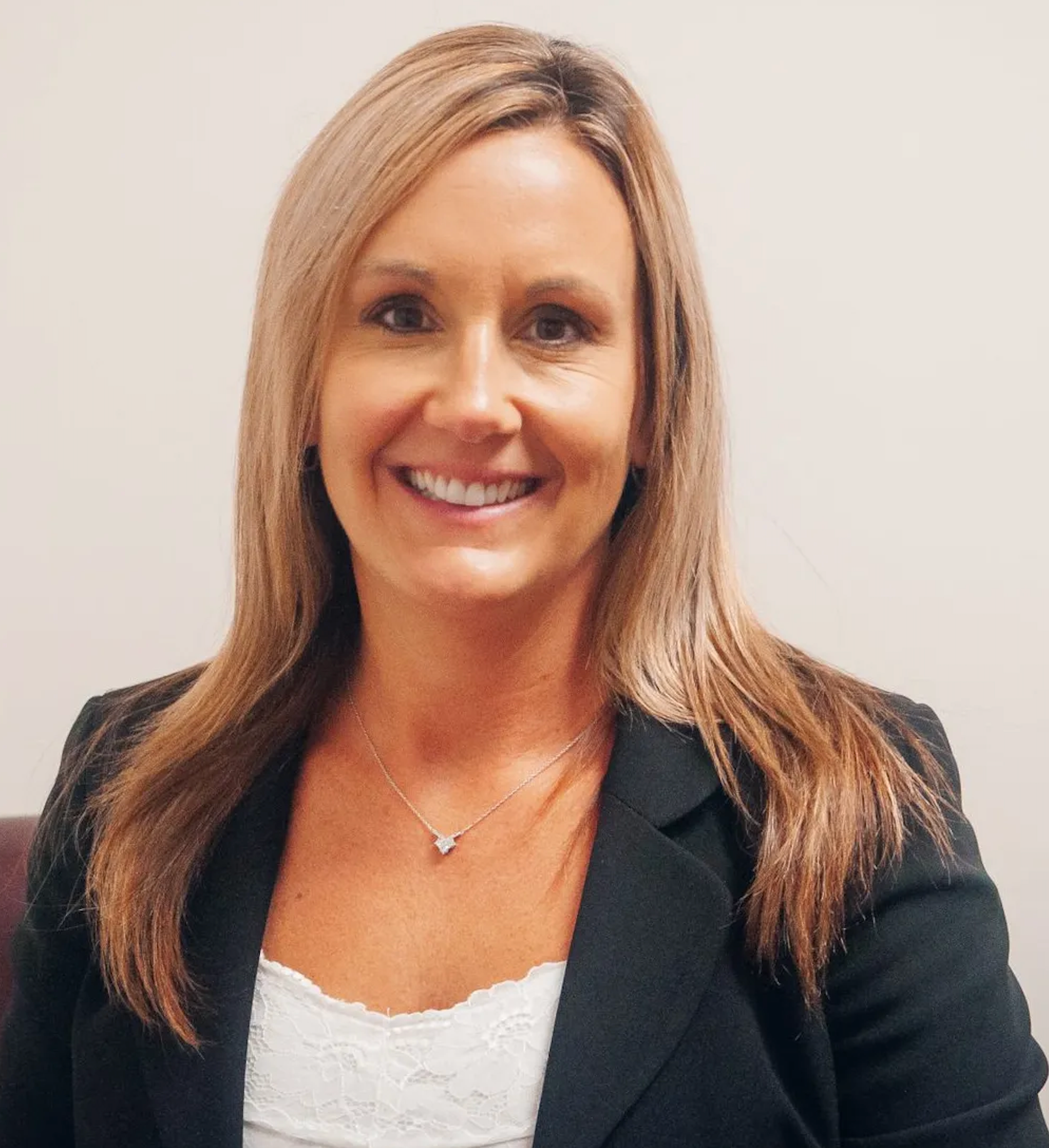 A woman wearing a black jacket and a white top smiles for the camera
