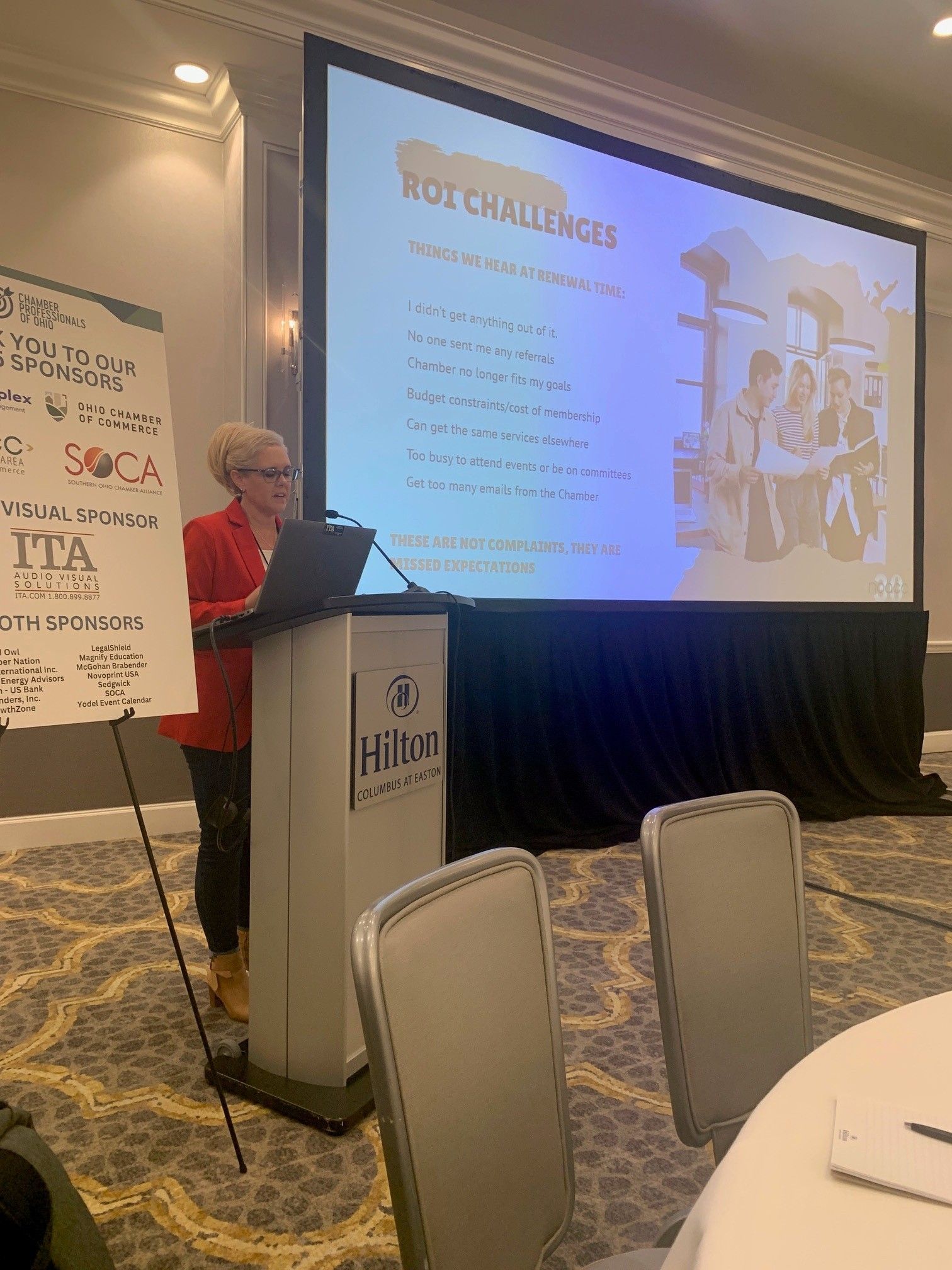 A woman is standing at a podium giving a presentation in front of a large screen.