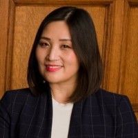 Woman in a navy blazer smiles at the camera, indoors in front of a wooden wall.