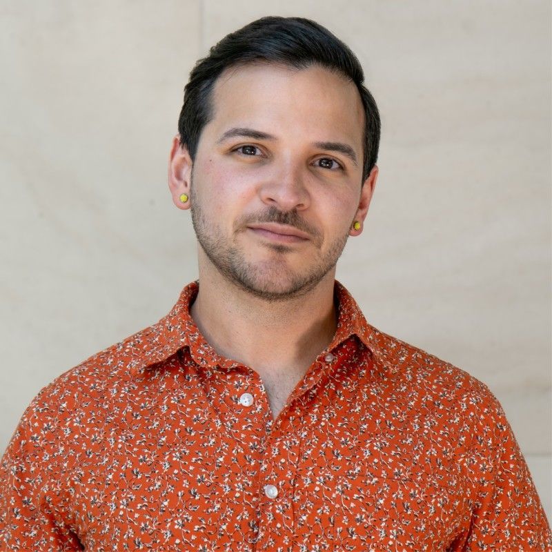 Man in an orange patterned shirt, small gold earrings, looking at the camera.