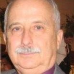 Man with a mustache wearing a purple shirt and gray blazer, looking at the camera.