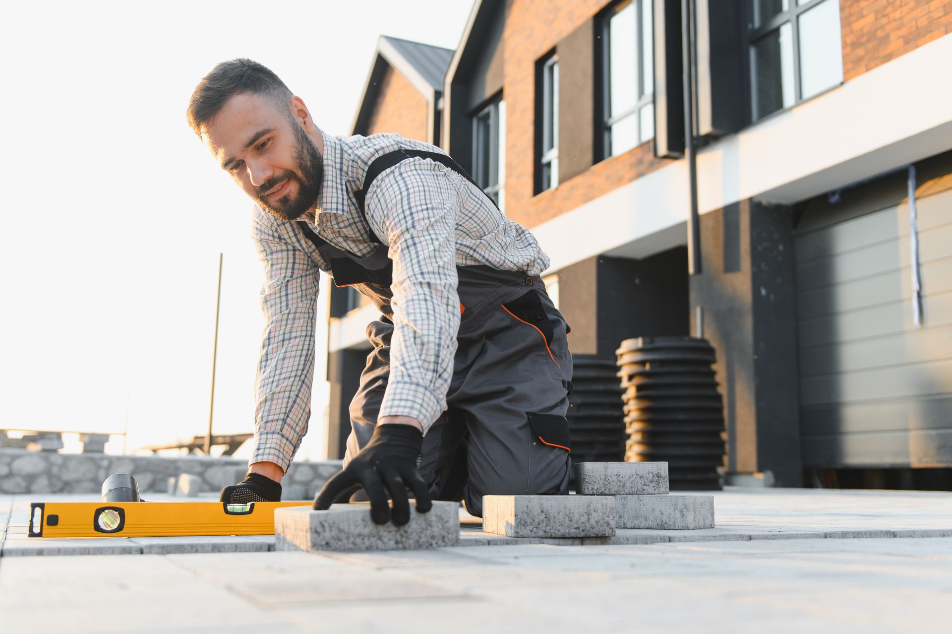 Worker installing paving stones and using a level outside a modern home. Worker installing paving stones and using a level outside a modern home.