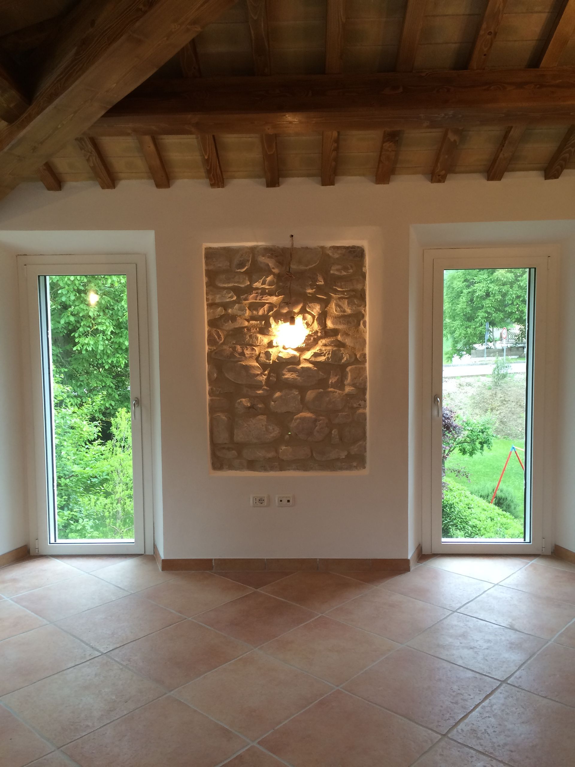 una stanza vuota con due finestre e un muro di pietra