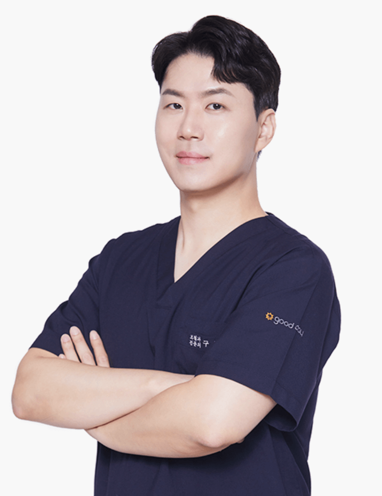 Smiling Asian man in navy blue scrubs with arms crossed. Medical setting.