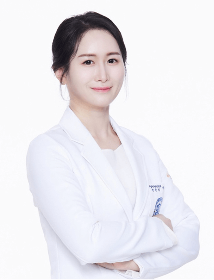 A smiling woman with dark hair in a white lab coat, arms crossed, against a white background.