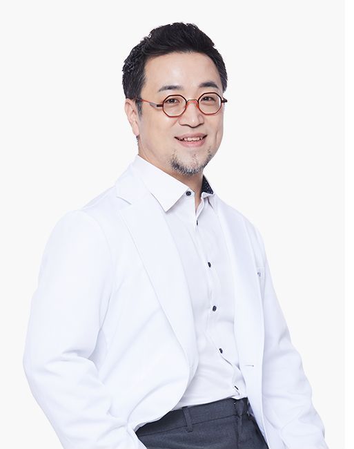 Smiling man in a white lab coat and glasses. He is standing in a white setting.