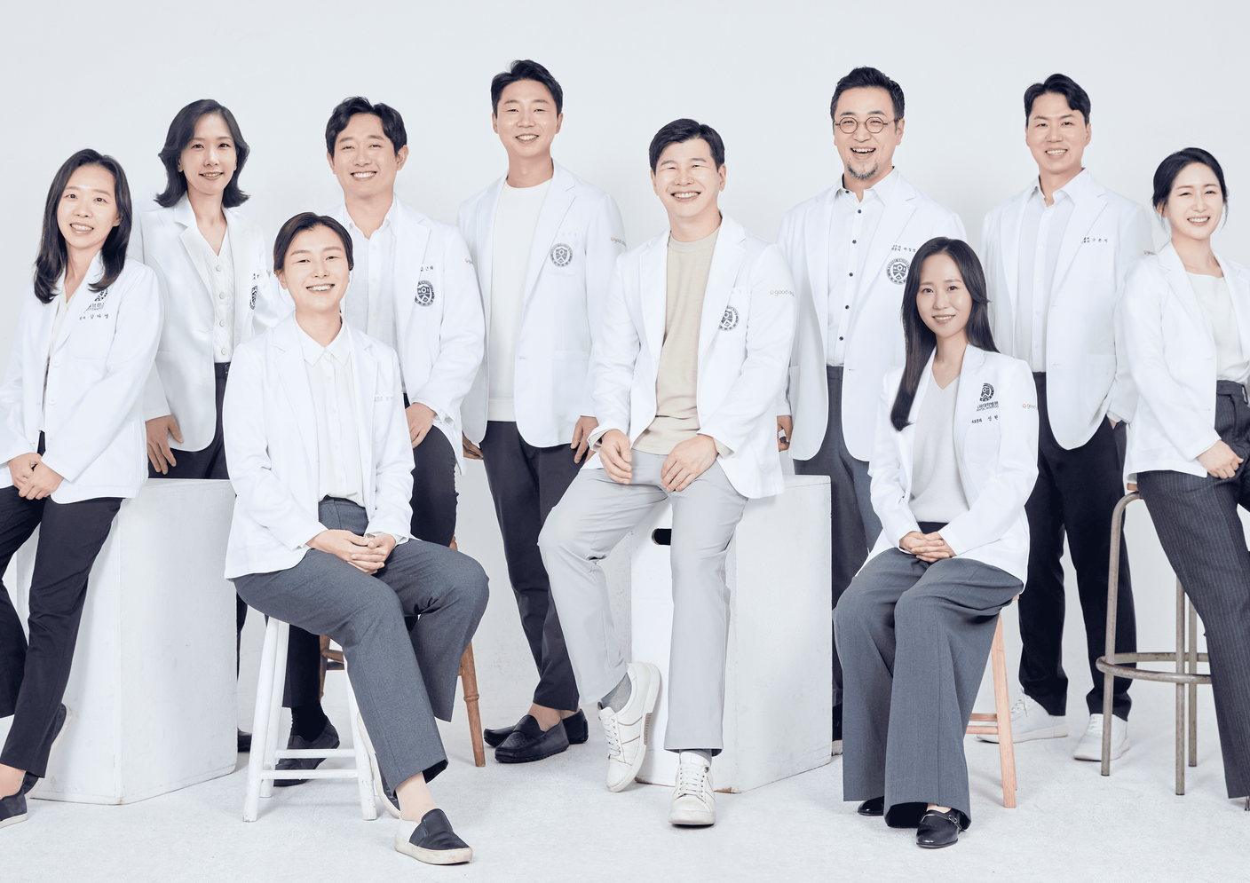 Group of eleven people in white coats and matching outfits posing against a white background. They appear to be health professionals.