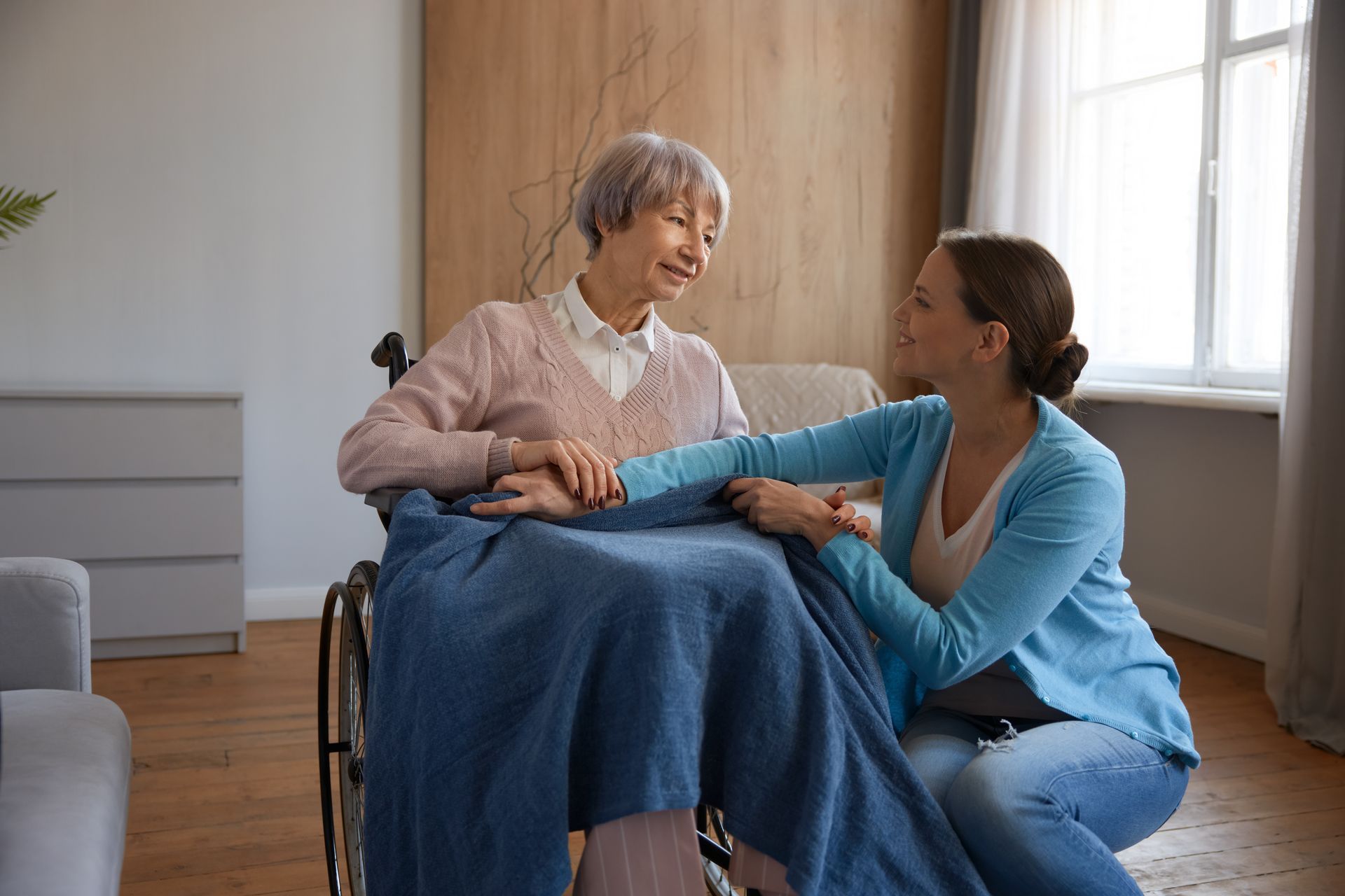 A woman is kneeling down next to an elderly woman in a wheelchair.