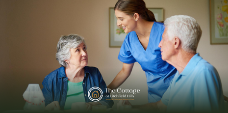Nurse in blue scrubs speaking with two older adults in an assisted living facility